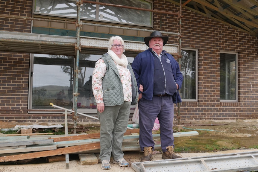 man and woman stand in front of job site with scaffolding 