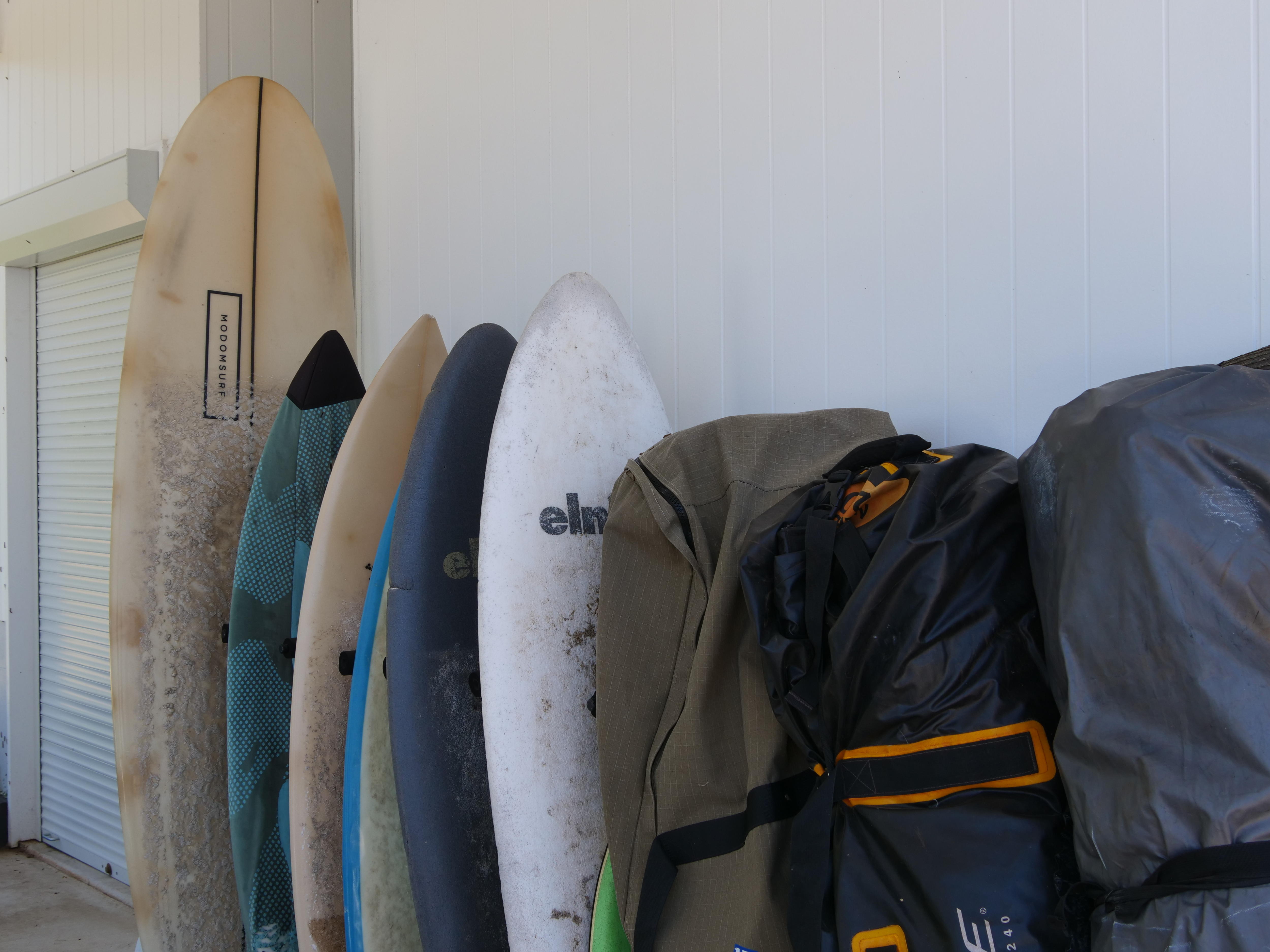 Estante de tablas de surf apiladas verticalmente en la pared de una casa, algunas de ellas en cajas.