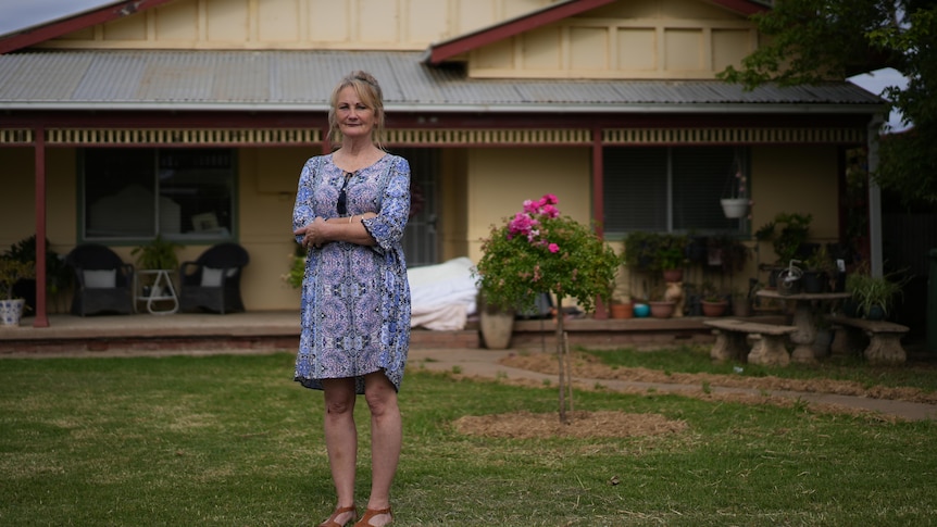 Woman wearing blue dress standing outside a house. 