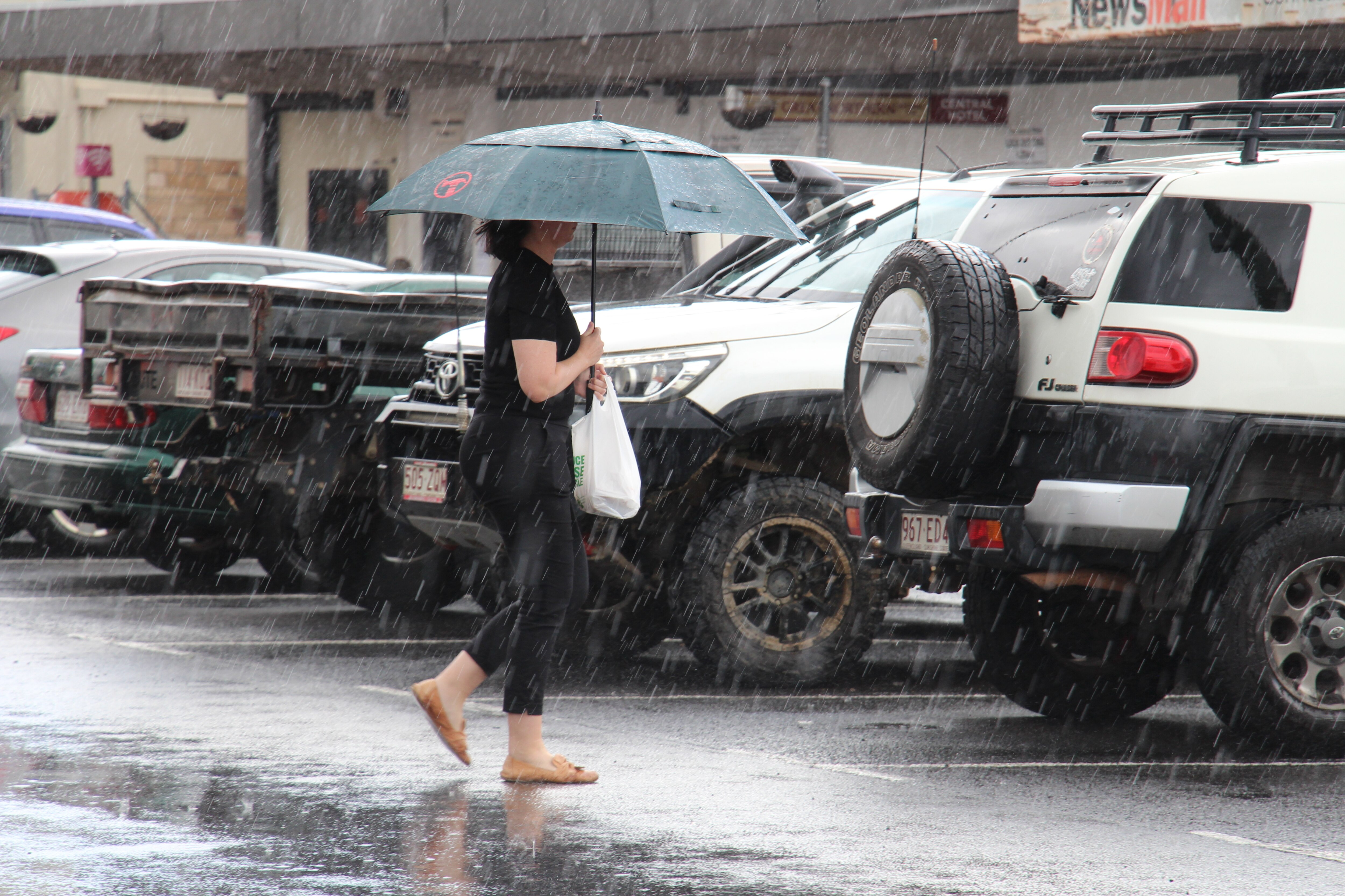A woman walks towards a row of cars with an umbrella over her head.