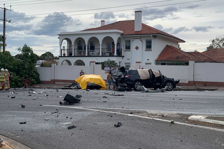 A crash scene outside a large white house. A fence is damaged and debris is strewn across the road.