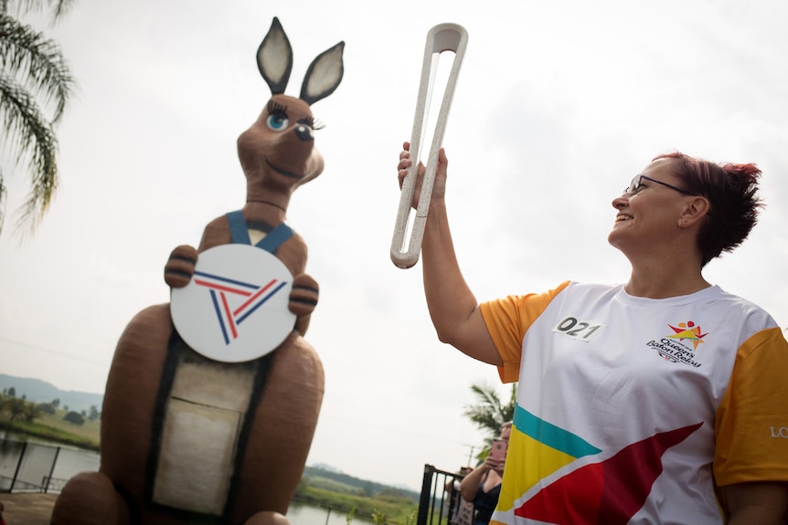 Natalie Upshall holding the Queen's Baton in front of Matilda the mascot