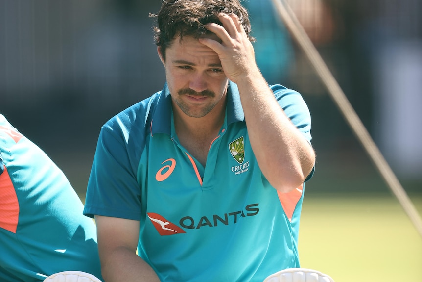 Travis Head scratches his head wearing training kit and pads