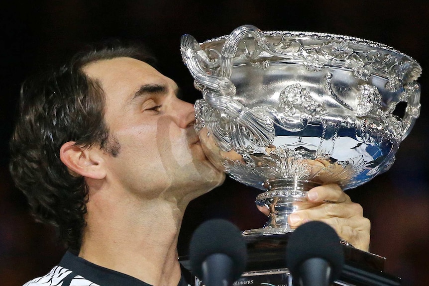 Roger Federer kisses the Australian Open trophy.