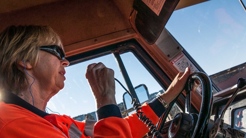 .A female truck driver holding a radio transmitter while behind the wheel.