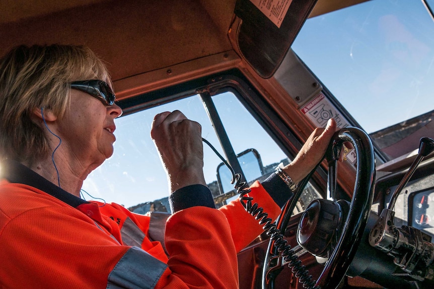 .A female truck driver holding a radio transmitter while behind the wheel.