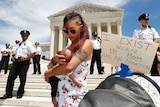 A woman holds her baby daughter on the Supreme Court steps next to a sign that says "I exist because my Mom had an abortion"