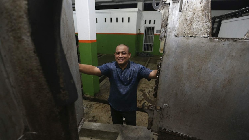 A man smiles as he opens the doors to a metal restraint box inside an empty abattoir.