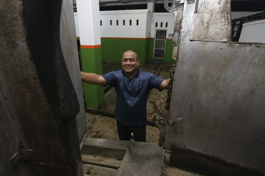 A man smiles as he opens the doors to a metal restraint box inside an empty abattoir.