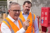 Two men in orange hi vis vest, with one holding up a dollar coin