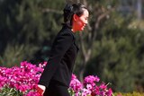 Wearing a suit, Kim Yo-jong walks past a flower garden.