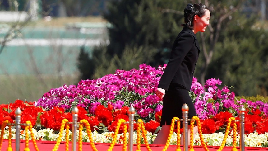 Wearing a suit, Kim Yo-jong walks past a flower garden.