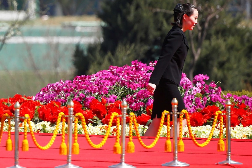 Wearing a suit, Kim Yo-jong walks past a flower garden.