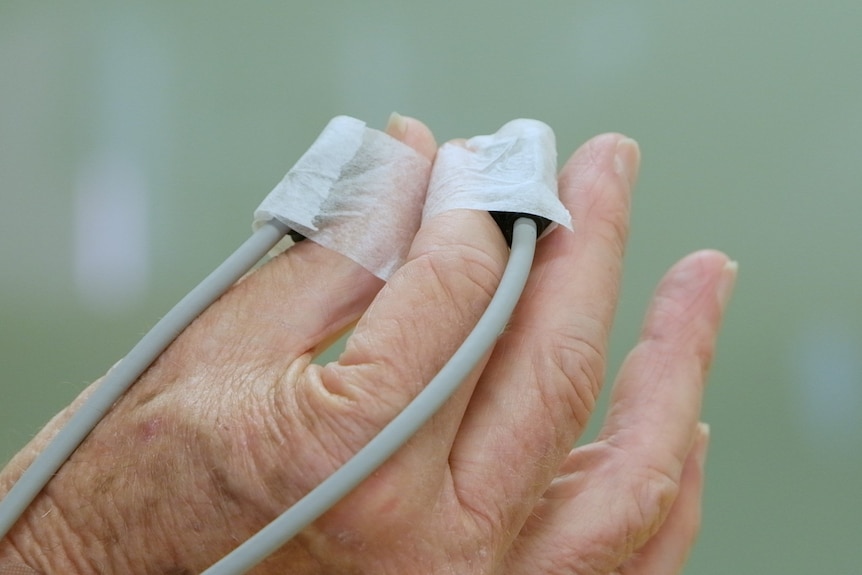 An older man's hand with medical wires attached to two of his fingers.