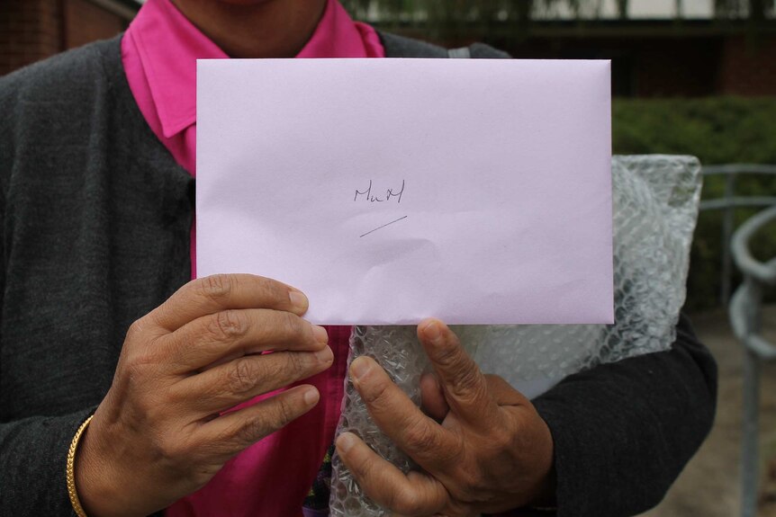 A close-up shot of a woman's hands holding a white card envelope with 'Mum' written on it.