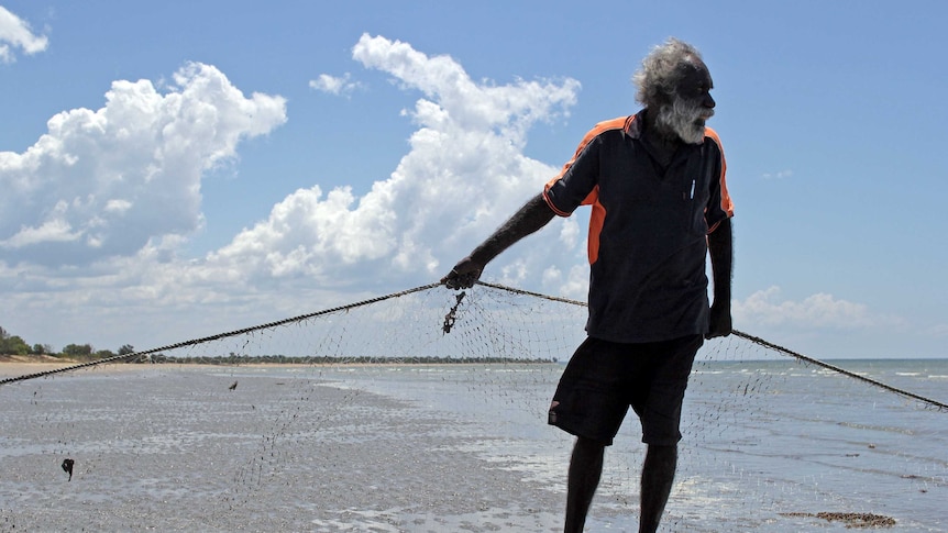 a man holding a net on a beach with clouds behind.