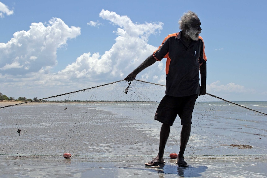 a man holding a net on a beach with clouds behind.