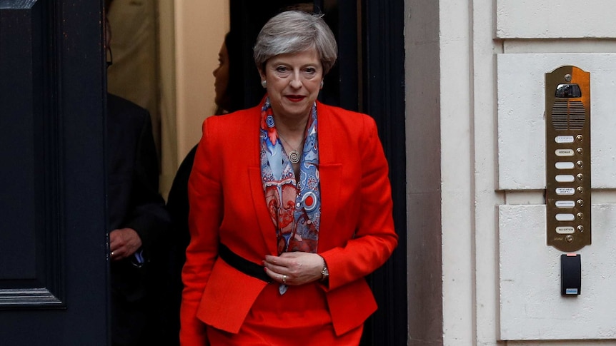 Theresa May walks out the front door of the headquarters wearing a red suit
