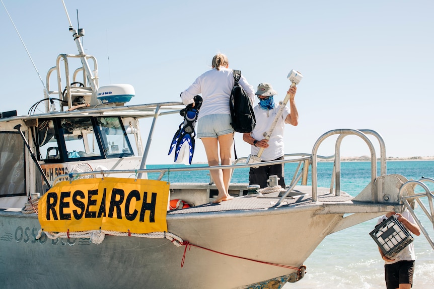 Two researchers standing on a boat on a beach on Western Australia's arid north west coast