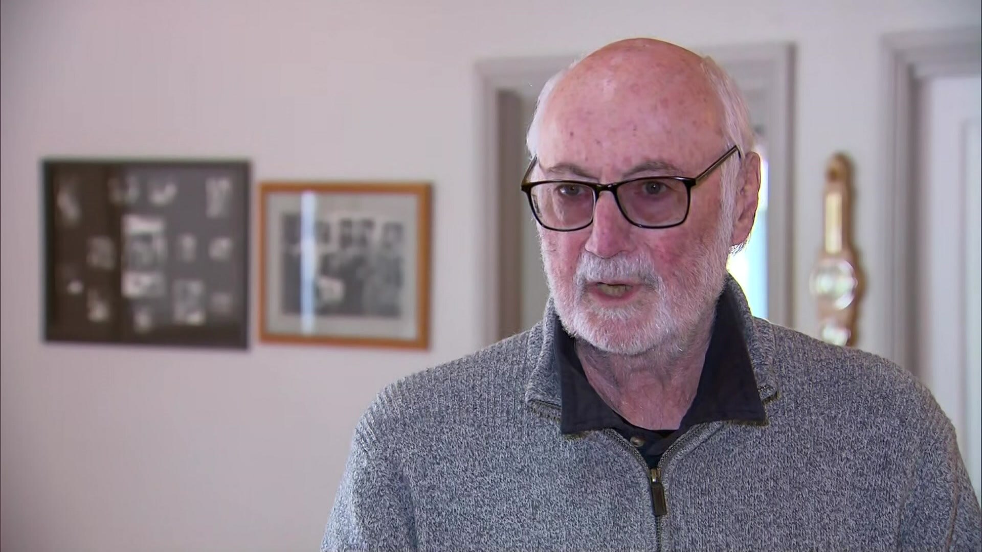 a man with glasses wearing a gray jumper.