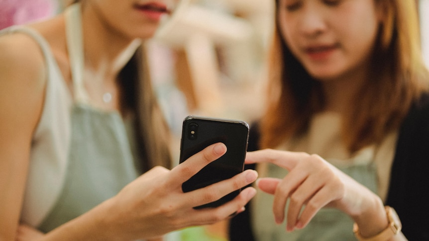 Two women who are out of focus look at something on a mobile phone.