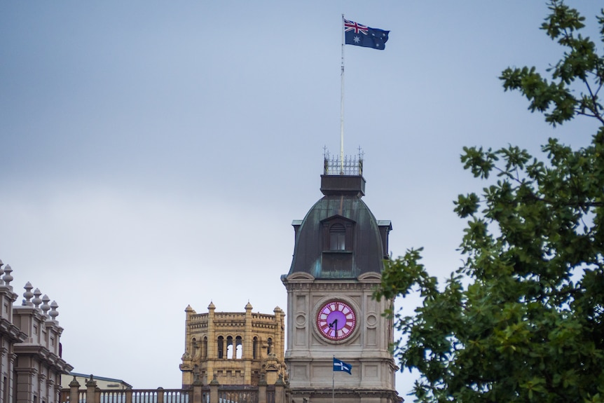 a tall building with a clock, an Australian flag on a pole and a eureka flag