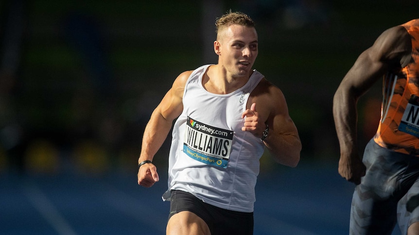 Trae Williams looks to his left as he crosses the finish line in a 100 metres race.