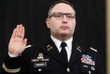 A middle aged army officer hold his right hand up with palm facing out and looks straight ahead as he swears an oath.
