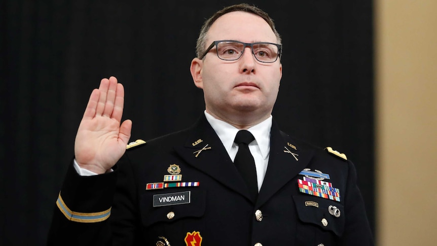 A middle aged army officer hold his right hand up with palm facing out and looks straight ahead as he swears an oath.
