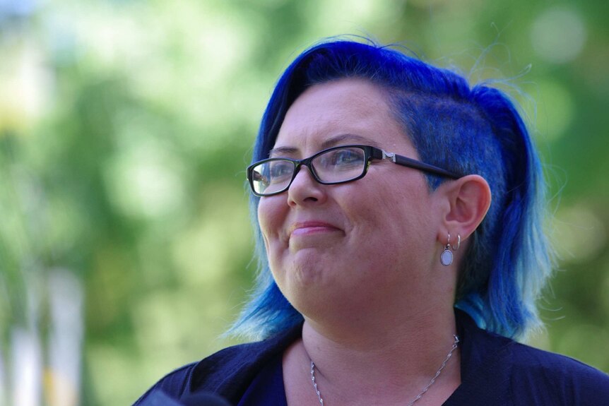 A tight head shot of a woman with blue hair outside.