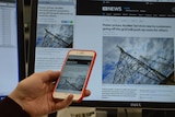 Mobile phone with news story on screen in front of computer screen with same story.