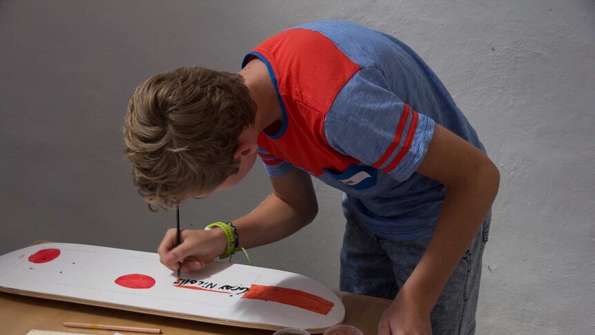 A boy painting a cricket bat on a skateboard deck
