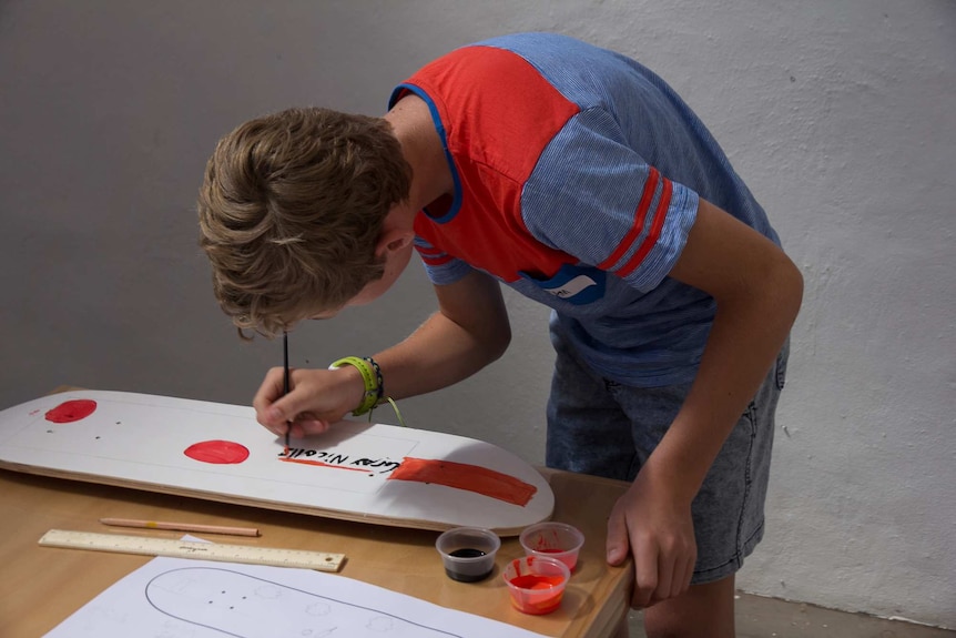 A boy painting a cricket bat on a skateboard deck