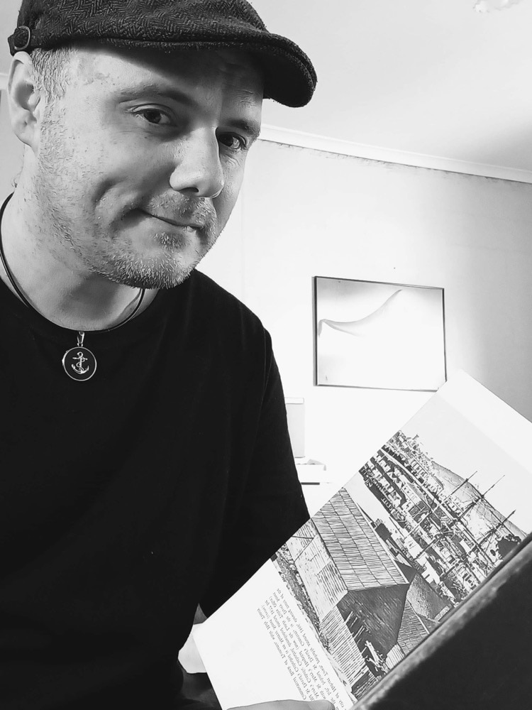 A man in a hat hold a book and look at the camera.