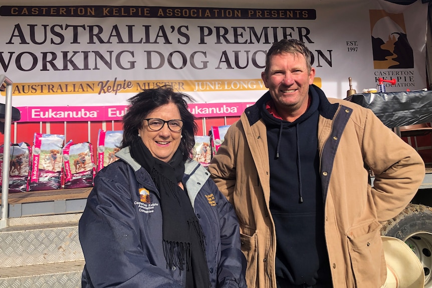 A middle-aged woman and man stand in front of an Australia's Premier Working Dog Auction sign