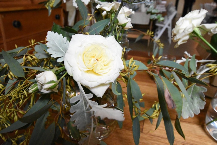 A bunch of white roses sitting on a table at the Euroa Butter Factory wedding venue.