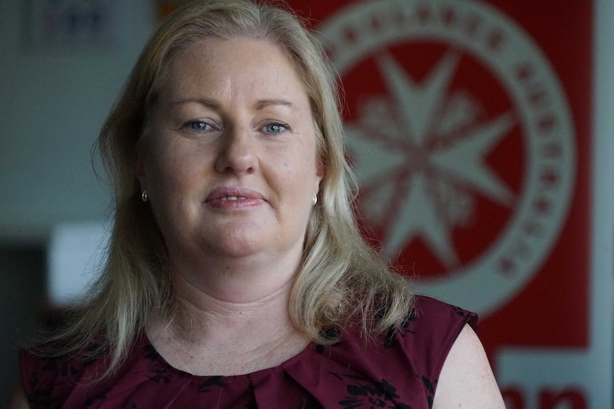 Judith Barker looks seriously at the camera. Behind her is a St John Ambulance NT logo.