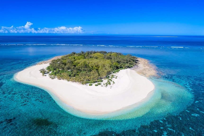 A secluded island surrounded by blue water and coral reef.