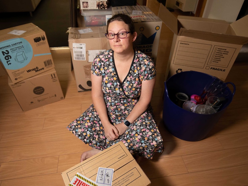 Kellee sits on the floor among cardboard boxes.