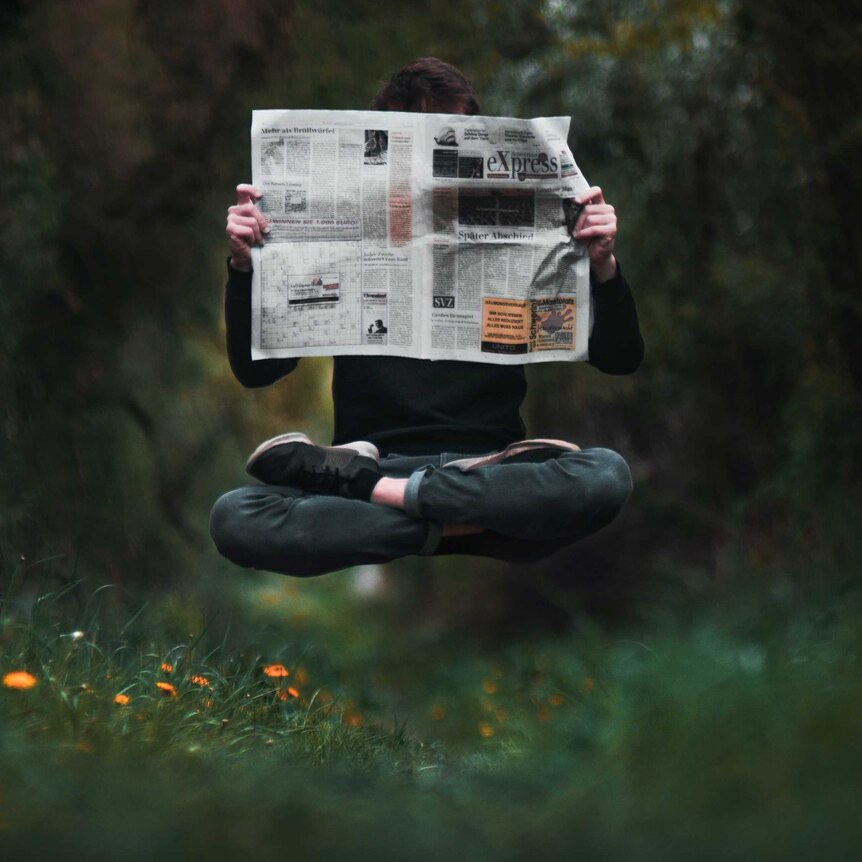 A person holds a newspaper while floating above the ground