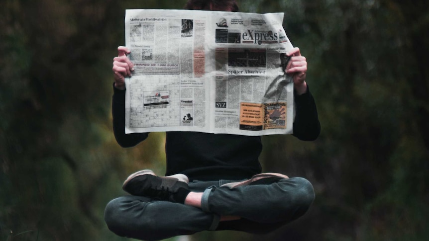 A person holds a newspaper while floating above the ground