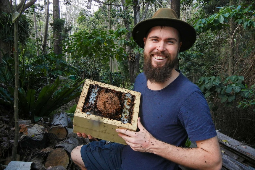 Bee researcher Dr Tobais Smith holds small home-made bee hive covered in native bees.