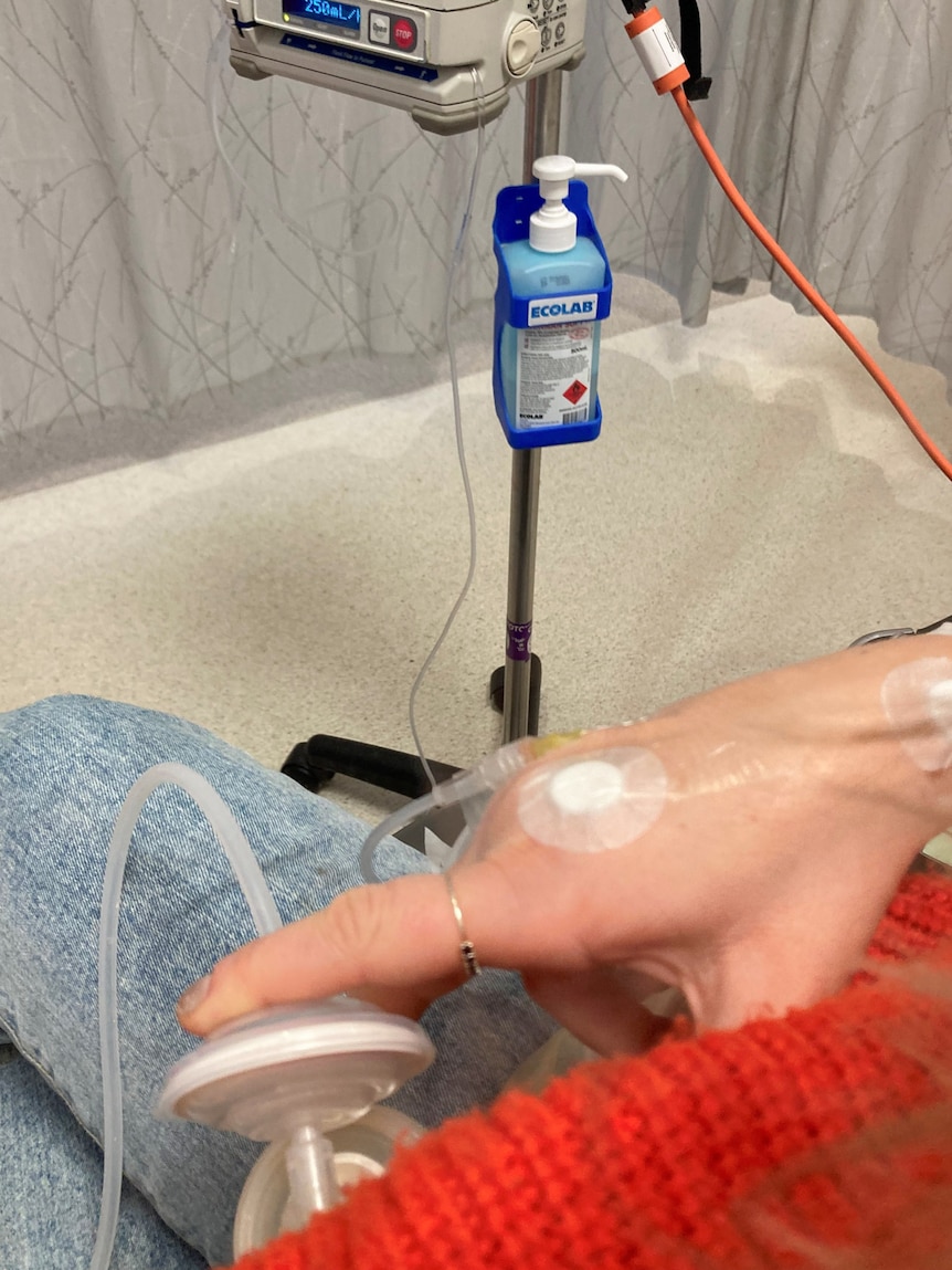 Close up of hand holding a breast pump while hooked up to drug infusion machine via cannula in the back of hand