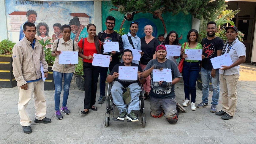 A group of 12 participants and trainers holding their training certifiicates smiling at the camera