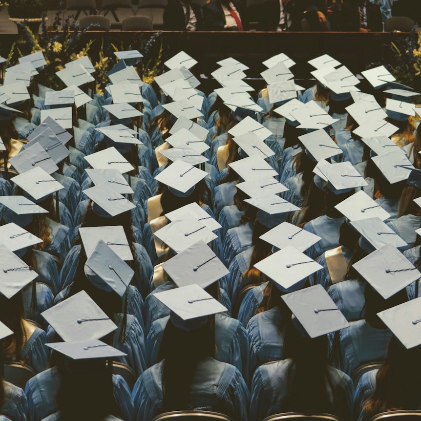 University students sitting on chairs at their graduation with a blue cap and gown on