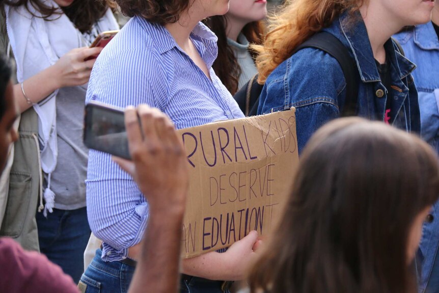 Protester holds a sign reading: rural kids deserve an education.