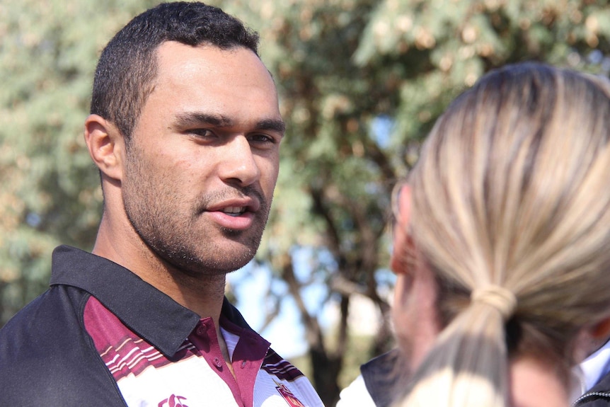 Tight headshot of Justin O'Neill speaking to reporters, the head of one out of focus in the foreground.