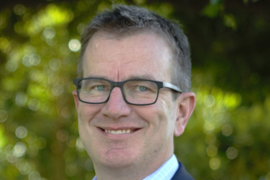 Down Syndrome Australia CEO Darryl Steff smiles at the camera with trees in background.