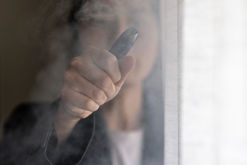 a woman holding onto a vape inside a room amid a cloud of smoke