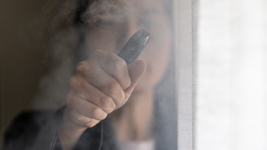 a woman holding onto a vape inside a room amid a cloud of smoke